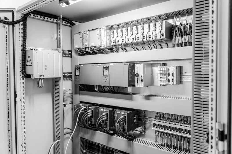 An open electrical control cabinet with rows of controllers, network switches, terminal blocks and labelled wires.