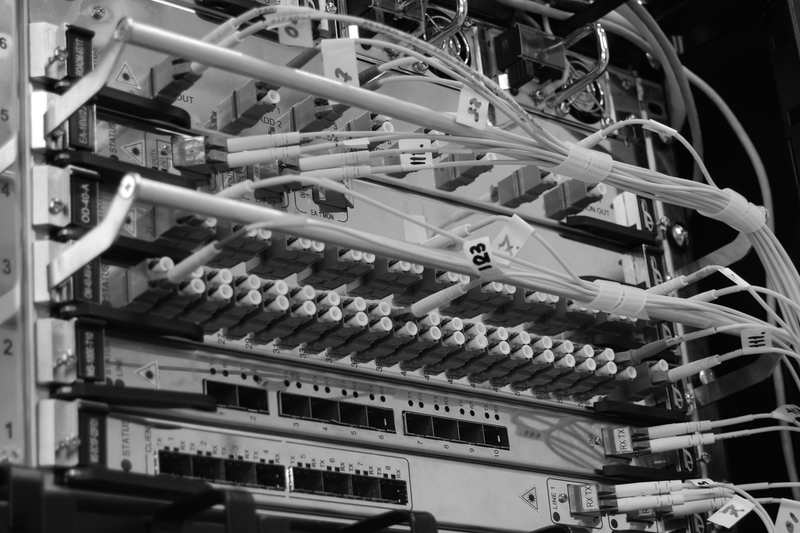 Close-up of fibre-optic cables plugged into rows of connectors in an equipment rack, each cable tagged with a handwritten number.